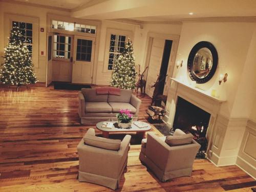 Cozy living room with two armchairs, a coffee table, and Christmas trees, featuring a fireplace and warm wooden floors.