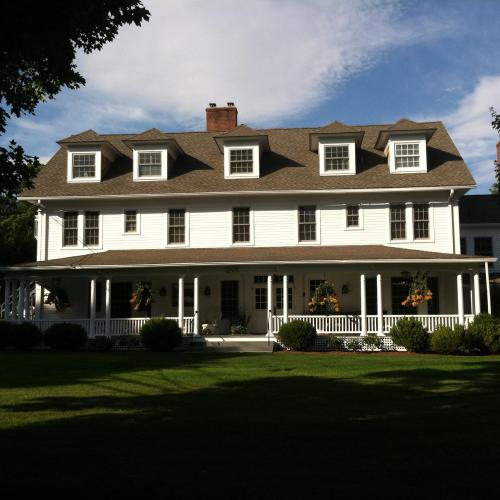 A large white house with multiple gables, a porch, and well-maintained landscaping under a clear blue sky.