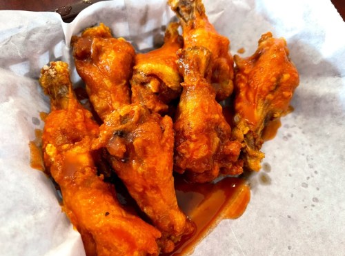 A close-up of spicy chicken wings coated in orange sauce, served on a piece of parchment paper.