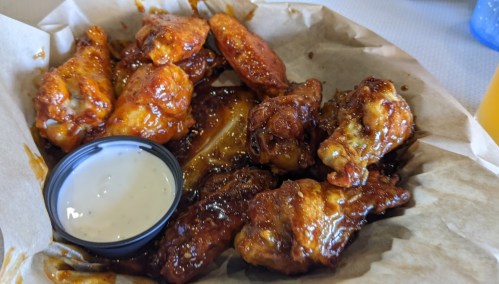 A basket of saucy chicken wings with a side of ranch dressing.