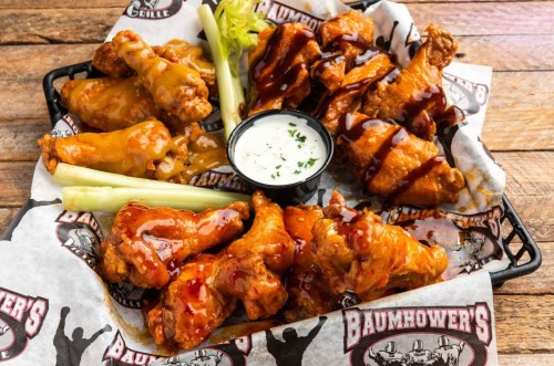 A platter of assorted chicken wings with sauces, celery sticks, and a side of ranch dressing on a wooden table.