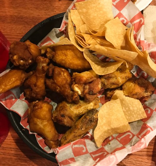 A plate of assorted chicken wings and crispy tortilla chips on a red and white checkered paper.