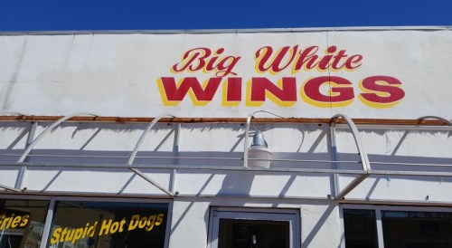 Sign on a building reads "Big White WINGS" in bold red and yellow letters against a white background.