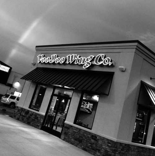 Black and white image of VooDoo Wing Co. restaurant exterior with a cloudy sky above.