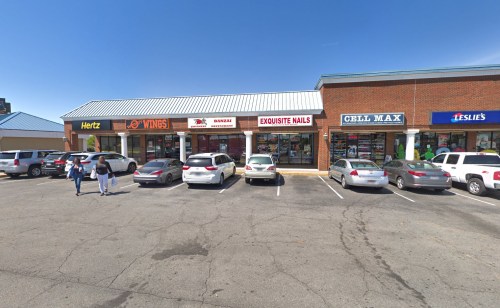 A row of businesses with a parking lot, featuring signs for Hertz, Wings, Exquisite Nails, Cell Max, and Leslie's.