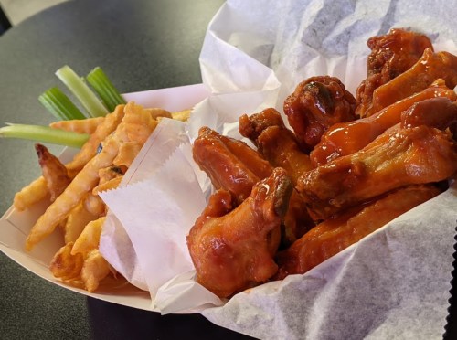 A serving of crispy chicken wings coated in sauce, accompanied by crinkle-cut fries and celery sticks.
