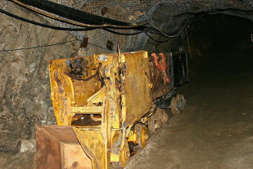 An old yellow mining cart sits in a dimly lit underground tunnel.