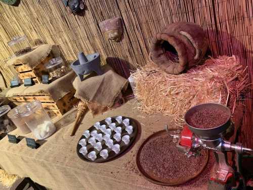 A rustic display featuring a grain grinder, cups, and various containers on a straw-covered table.