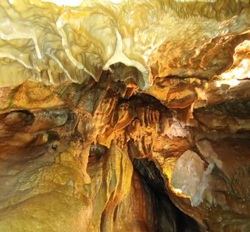 Stalactites and rock formations in a dimly lit cave, showcasing intricate textures and warm colors.