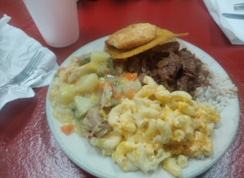 A plate of food featuring macaroni and cheese, beef, rice, a biscuit, and a vegetable stew on a red table.