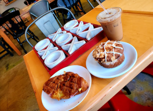 A table with a croissant sandwich, a muffin, and an iced coffee, with a tic-tac-toe game in the background.