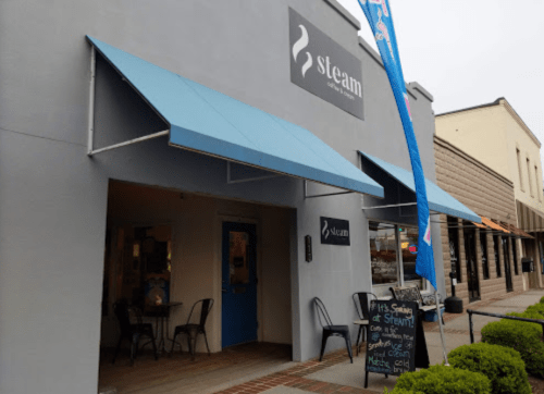 Exterior of a café named "Steam," featuring blue awnings and a chalkboard sign outside.