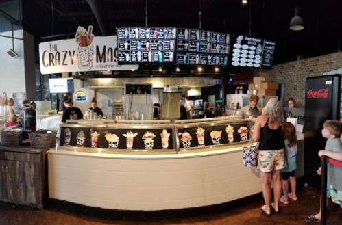 A busy ice cream shop with a menu board, customers at the counter, and a display of colorful ice cream treats.