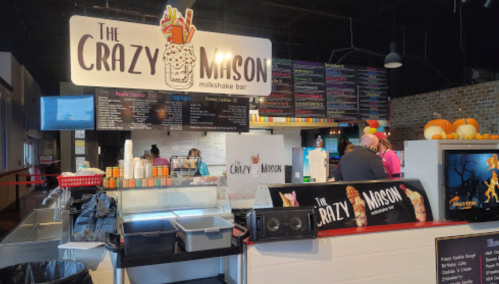 Interior of The Crazy Mason milkshake bar, featuring a colorful menu and customers ordering milkshakes.