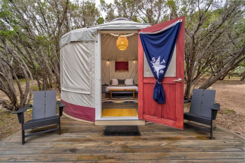 A cozy yurt with a red door, inviting seating outside, surrounded by trees and nature.