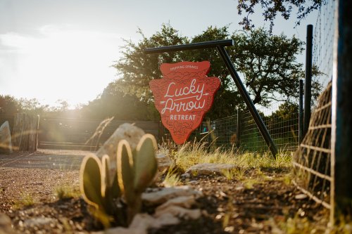 Sign for Lucky Arrow Retreat at sunset, surrounded by greenery and a cactus in the foreground.