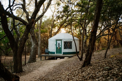 A cozy yurt nestled among trees, with a path leading to it, surrounded by autumn foliage.