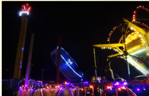 A vibrant night scene featuring colorful lights from a carnival ride and a tall tower with a glowing crown on top.