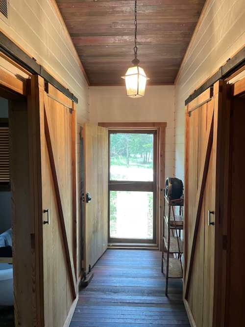 A hallway with wooden sliding doors, a window at the end, and a vintage lamp hanging from the ceiling.