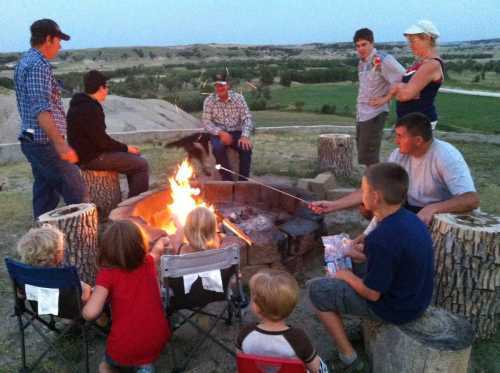 A group of people gathered around a campfire, roasting marshmallows and enjoying the outdoors in a scenic setting.