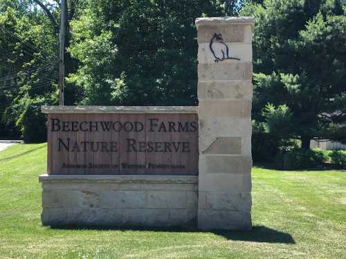 Sign for Beechwood Farms Nature Reserve, featuring a stone pillar and a small animal illustration, surrounded by greenery.