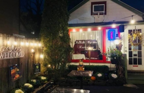 A cozy Italian restaurant exterior with warm lights, a "Welcome" sign, and a glowing "Open" neon sign.
