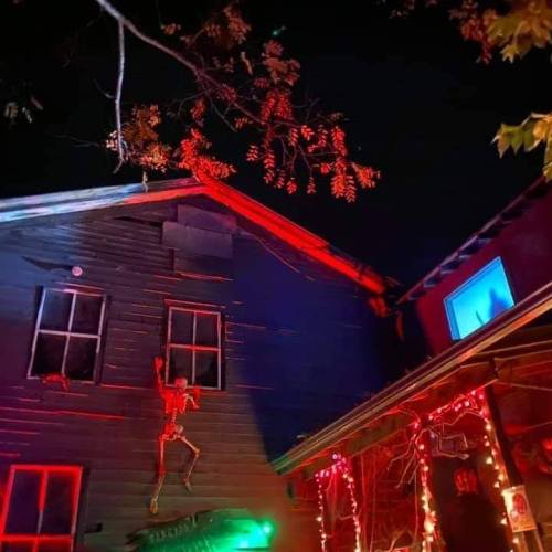A spooky house at night, featuring a skeleton decoration and colorful lights illuminating the exterior.