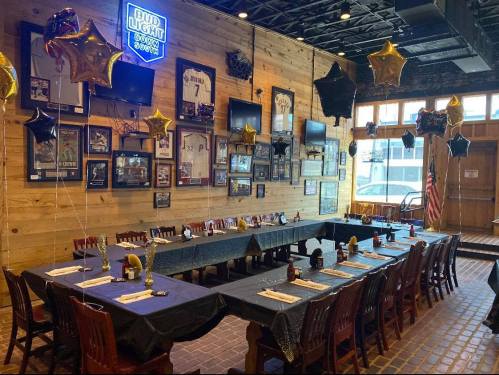 A decorated dining area with tables set for a gathering, featuring balloons, framed sports memorabilia, and a neon sign.