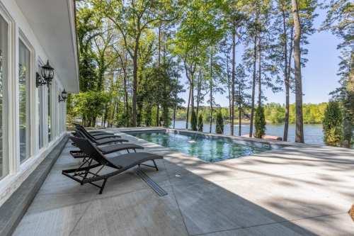 A serene lakeside view featuring a pool and lounge chairs surrounded by trees and greenery.