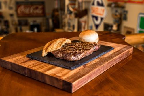 A perfectly grilled steak on a slate platter, accompanied by a toasted bun, set on a wooden table.