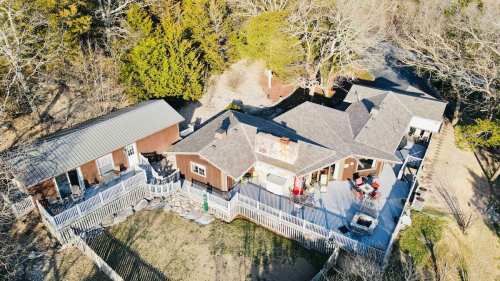 Aerial view of a spacious house surrounded by trees, featuring a large deck and outdoor seating area.