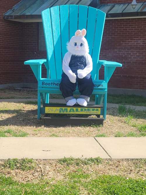 A large turquoise chair with a person in a bunny costume sitting on it, in front of a brick building.
