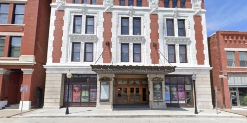 Historic theater building with ornate facade and marquee, featuring posters and a clear blue sky in the background.