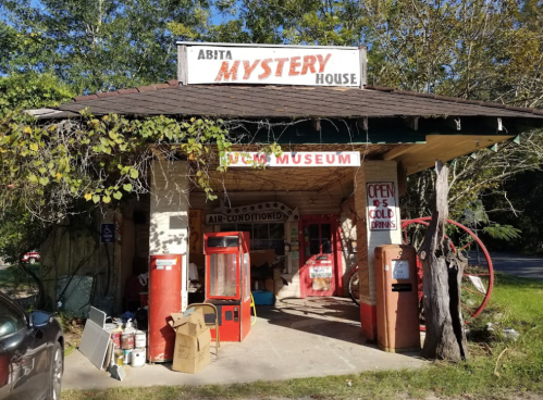 Abita Mystery House, a quirky museum with vintage signs and artifacts, surrounded by trees and a sunny sky.