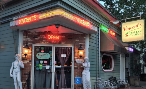 Exterior of Vincent's Italian Cuisine, featuring neon signs, an "Open" sign, and two statues flanking the entrance.