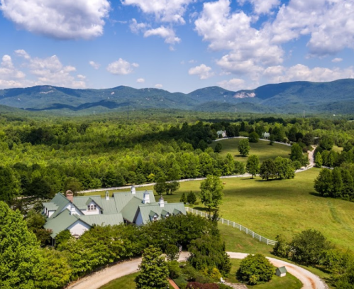 Aerial view of a green landscape with rolling hills, trees, and a winding road leading to a large house.