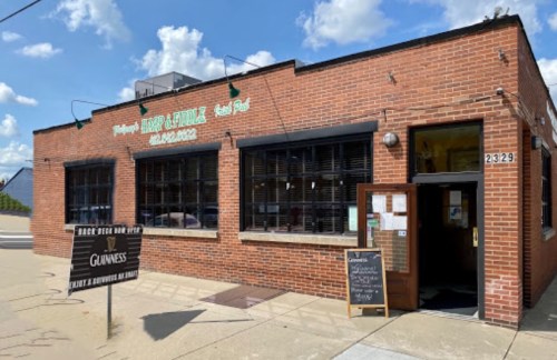 A brick building with large windows and a sign for a pub, featuring outdoor seating and a Guinness advertisement.