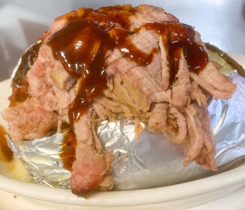 A baked potato topped with shredded meat and barbecue sauce, served in a foil wrapper.