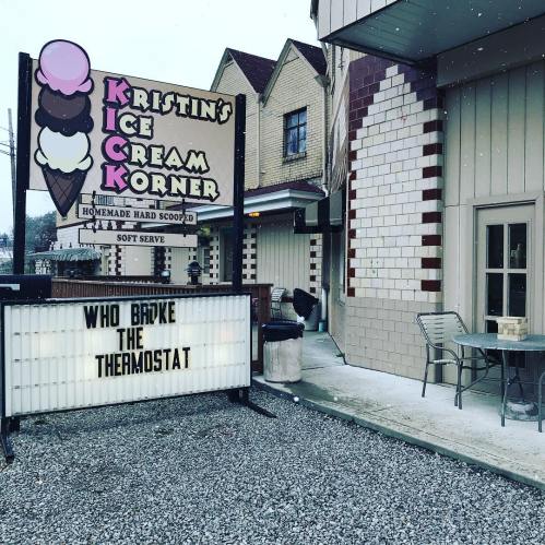 A colorful ice cream shop sign with a humorous message on a marquee about a broken thermostat, surrounded by snow.