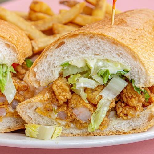 A close-up of a sandwich filled with fried chicken, lettuce, and pickles, served with a side of golden fries.