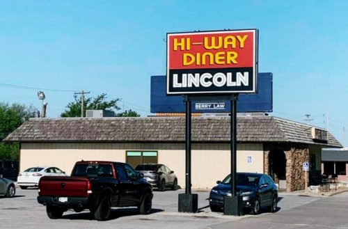 Sign for Hi-Way Diner in Lincoln, with a parking lot featuring a red truck and a black car. Clear blue sky above.