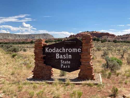 Sign for Kodachrome Basin State Park, surrounded by desert landscape and rocky formations under a blue sky.