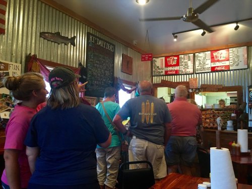 A group of people stands in line at a rustic restaurant, looking at the menu on the wall.