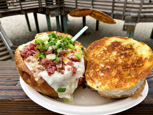 A hearty sandwich with creamy filling, topped with green onions and bacon, served on a toasted bun.