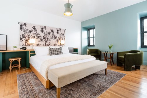 A modern bedroom featuring a large bed, green walls, a rug, and cozy seating areas with natural light.