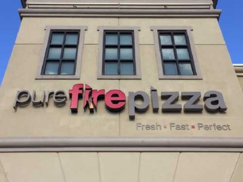 Sign for "pure fire pizza" with the tagline "Fresh - Fast - Perfect" on a building exterior.