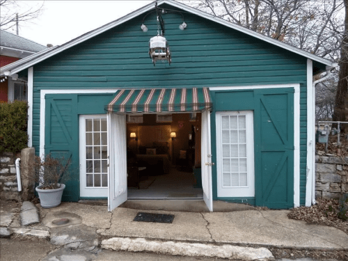 A green garage with double doors open, revealing a cozy interior and a striped awning above the entrance.