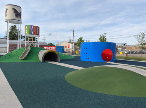 Colorful playground featuring a slide, tunnel, and climbing structures on green turf under a blue sky.