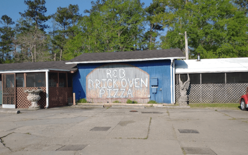 A rustic pizza restaurant with a blue exterior and large "R&B Brickoven Pizza" sign, surrounded by trees.