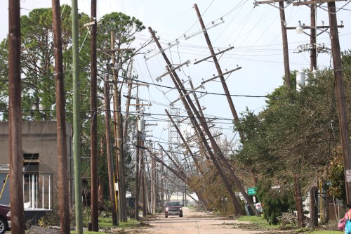 A street lined with leaning power poles and downed trees, indicating recent storm damage.